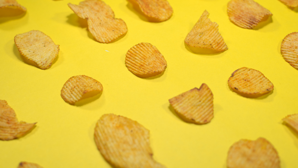 Multiple potato chips on yellow background. Image: Unsplash