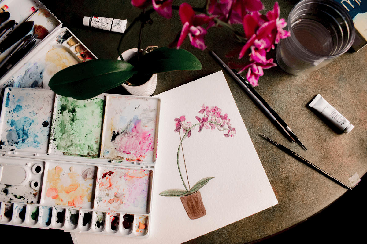 Watercolour set and painting of an orchid on a table